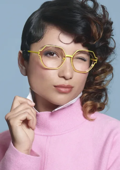 Portrait d'une femme portant des montures WOOW jaunes aux formes hexagonales, avec un pull rose.